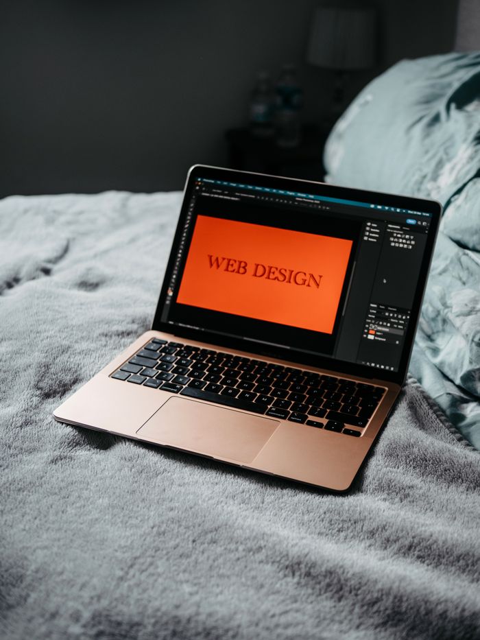 A laptop resting on a bed displays web design software, setting up a cozy workspace.